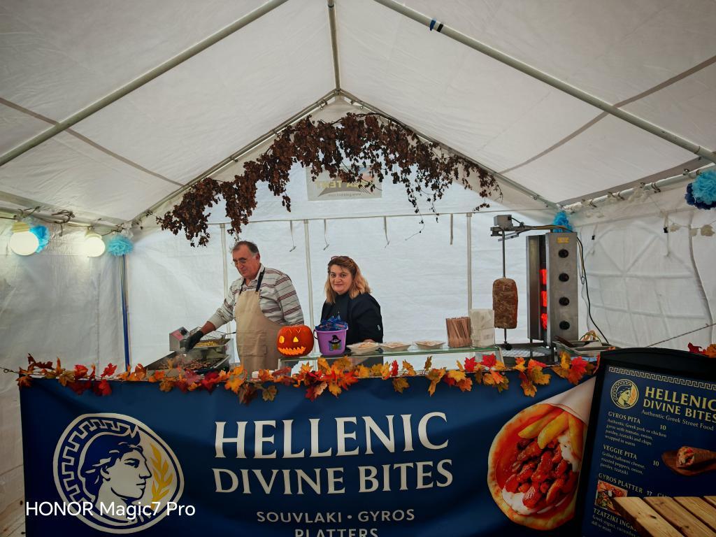 Authentic Greek food market stall set up under a white marquee in an autumn park.